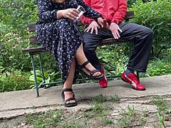 Hot mature MILF grabs huge cock for outdoor handjob. She milks cumshot into glass on park bench.