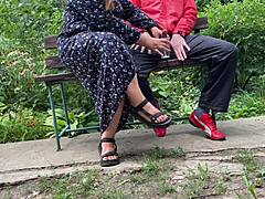 Hot mature MILF grabs huge cock for outdoor handjob. She milks cumshot into glass on park bench.